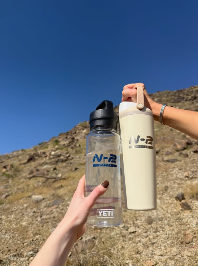 Two N-2 water bottles raised together on a desert trail
